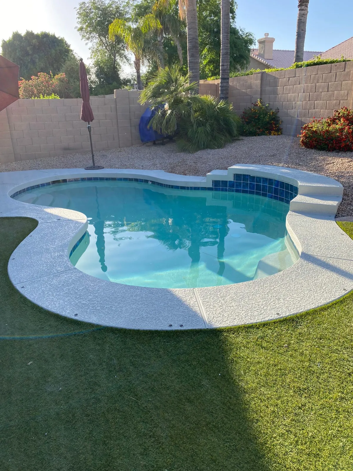 Freeform existing pool with raised sun shelf after a finished light interior, new tile, and renewed deck